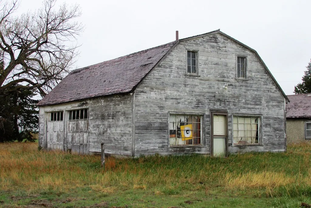 Old gray barn with broken windows in tall grass.