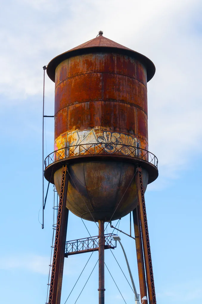 Old elevated metal tank covered in rust and graffiti.