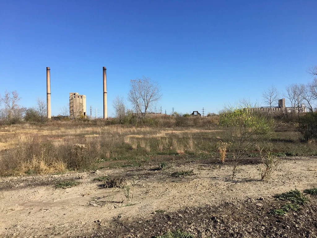 Deux cheminées et des vestiges industriels dans une friche.