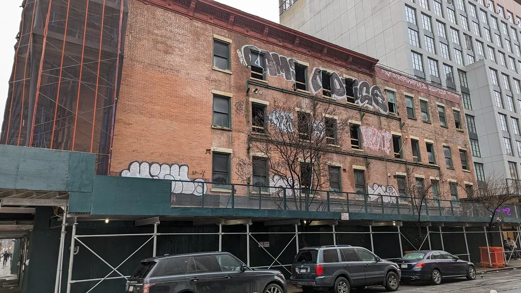 Immeuble de briques délaissé aux fenêtres brisées et façades couvertes de graffitis derrière un échafaudage.