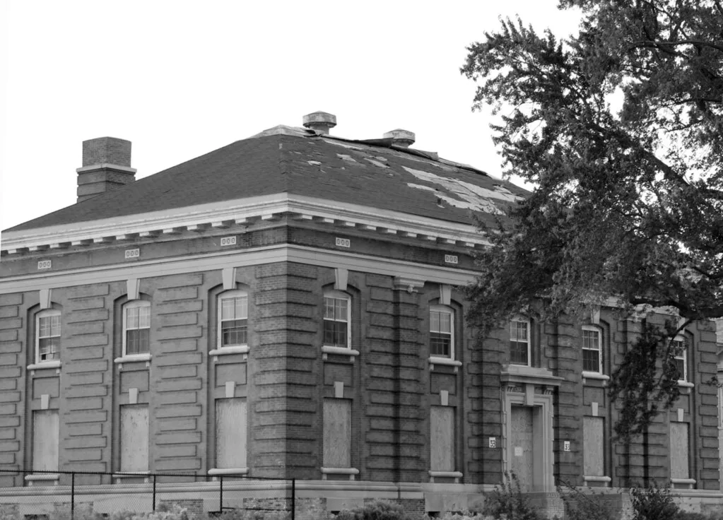 Old building with boarded lower openings and a deteriorated roof.