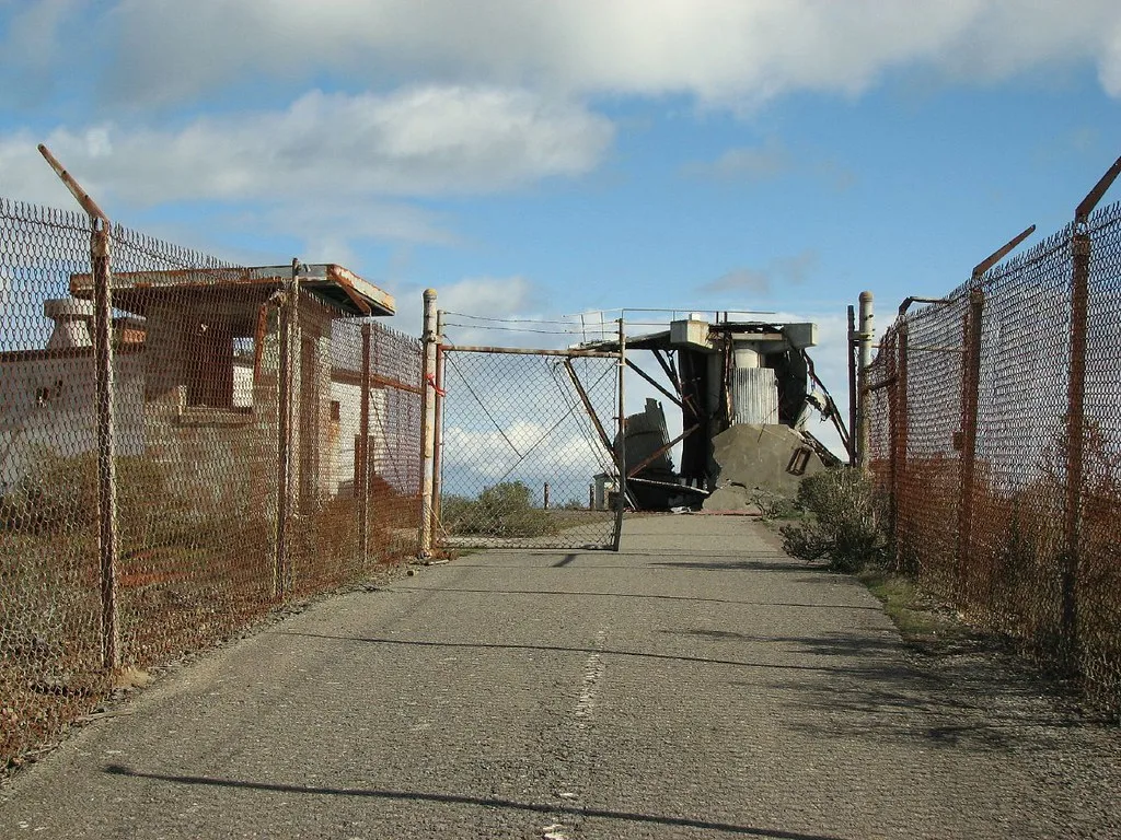 Old collapsed structures at the end of a fenced access path.
