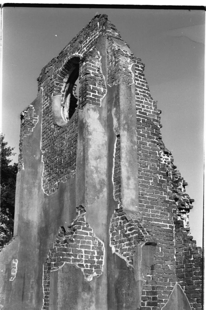 Ruined brick wall with a circular opening and peeling plaster, in black and white.