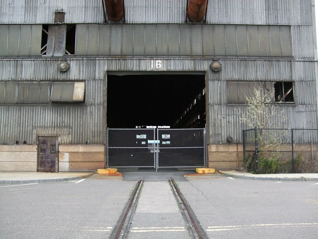 Gated entrance to an old industrial hall with broken windows.