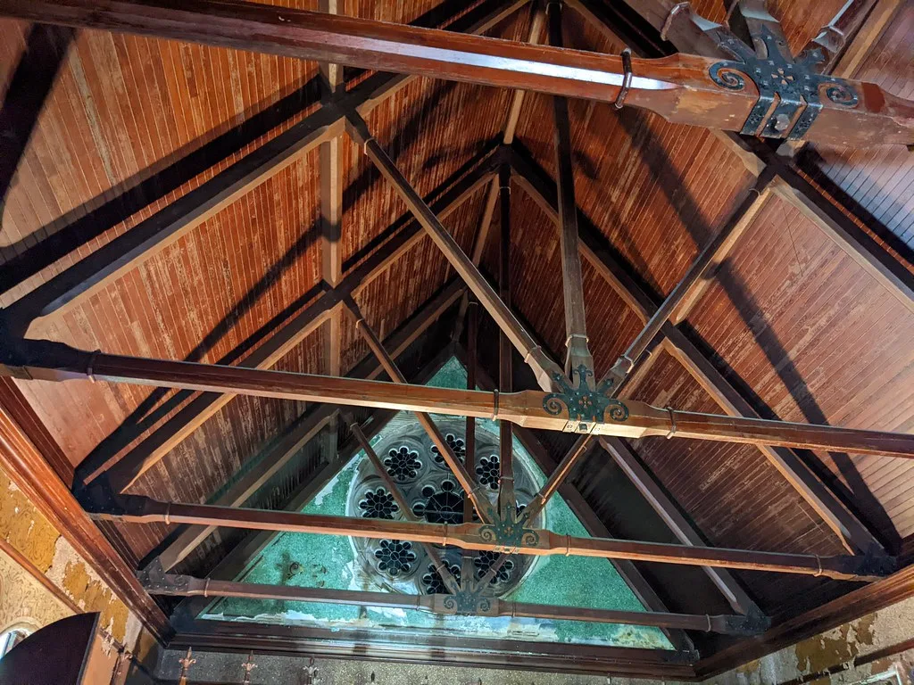 Charpente en bois au-dessus d’un vitrail dégradé et de murs écaillés.