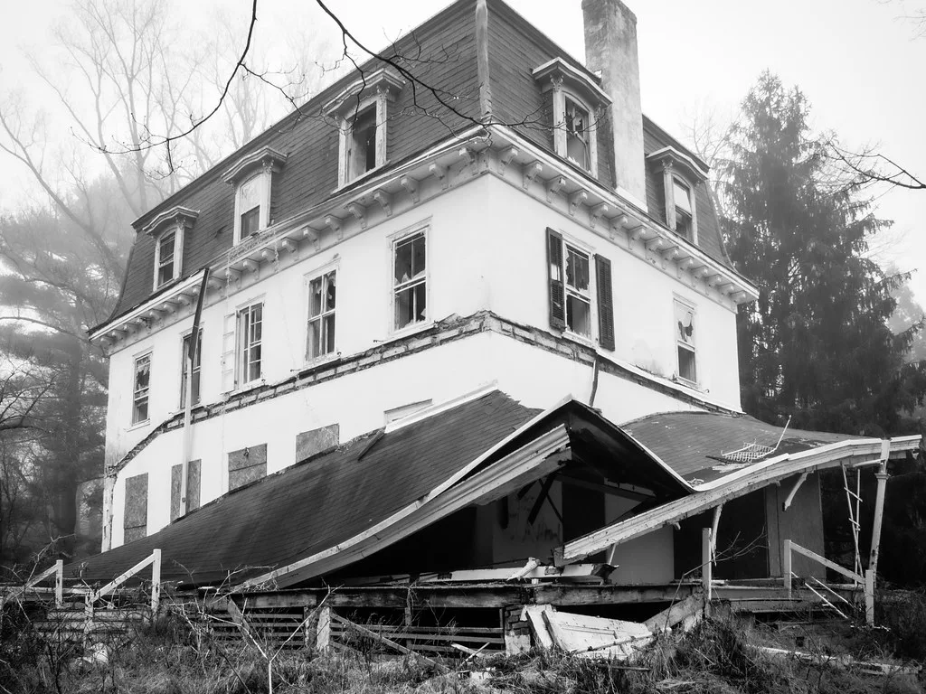 Old white building with broken windows and a collapsed porch.