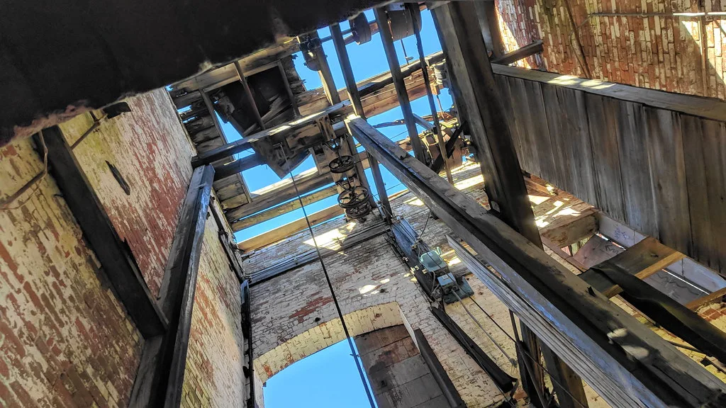 Timber framing and machinery in a gutted industrial building with sky visible through its floors.