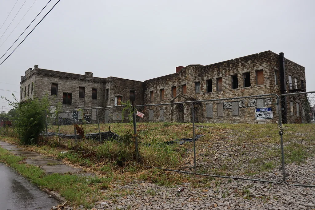 Old large stone building with empty windows behind a fence.