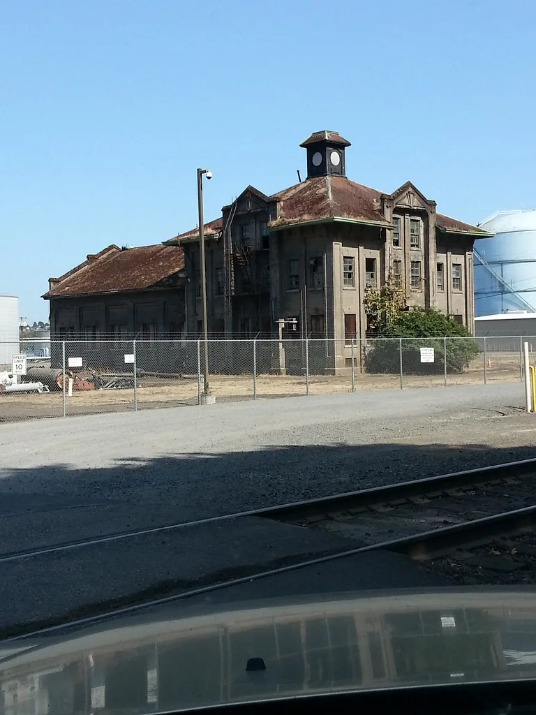 Abandoned industrial building with a cupola and red roof behind a wire fence.