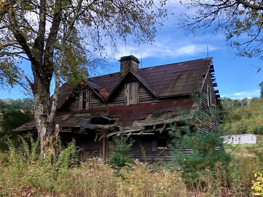 Ancienne maison en bois à la toiture de porche effondrée dans les hautes herbes.