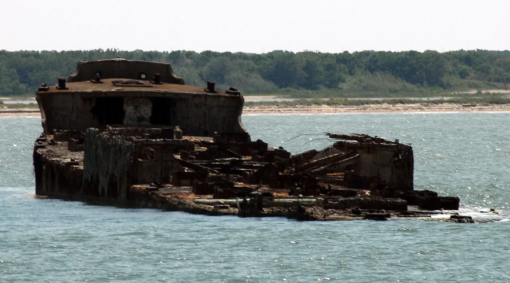 Rusty shipwreck partly submerged near a wooded shore.