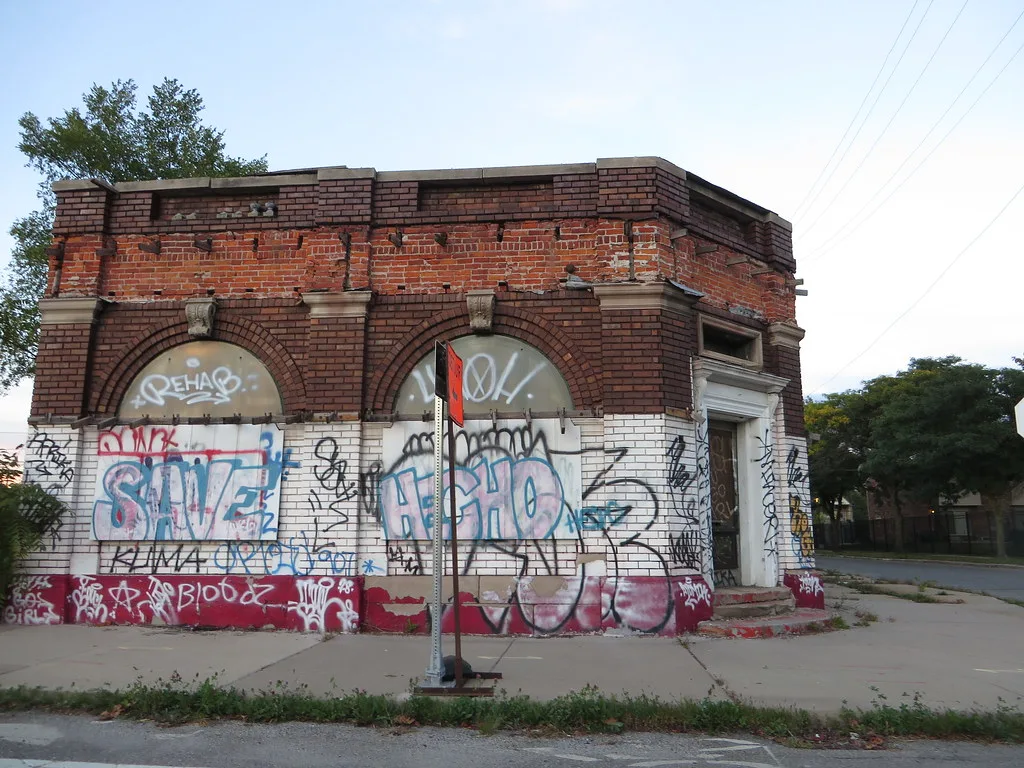 Small neglected brick building with large walled-up arched openings covered in graffiti.