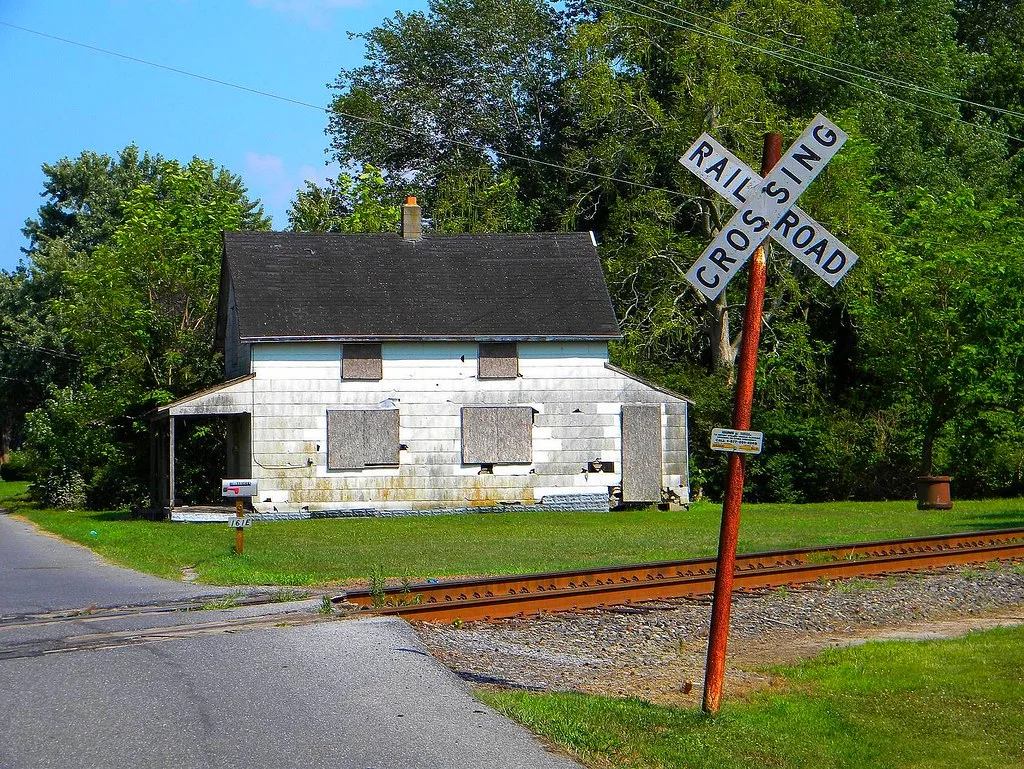 Old white house with boarded openings beside a railway track.