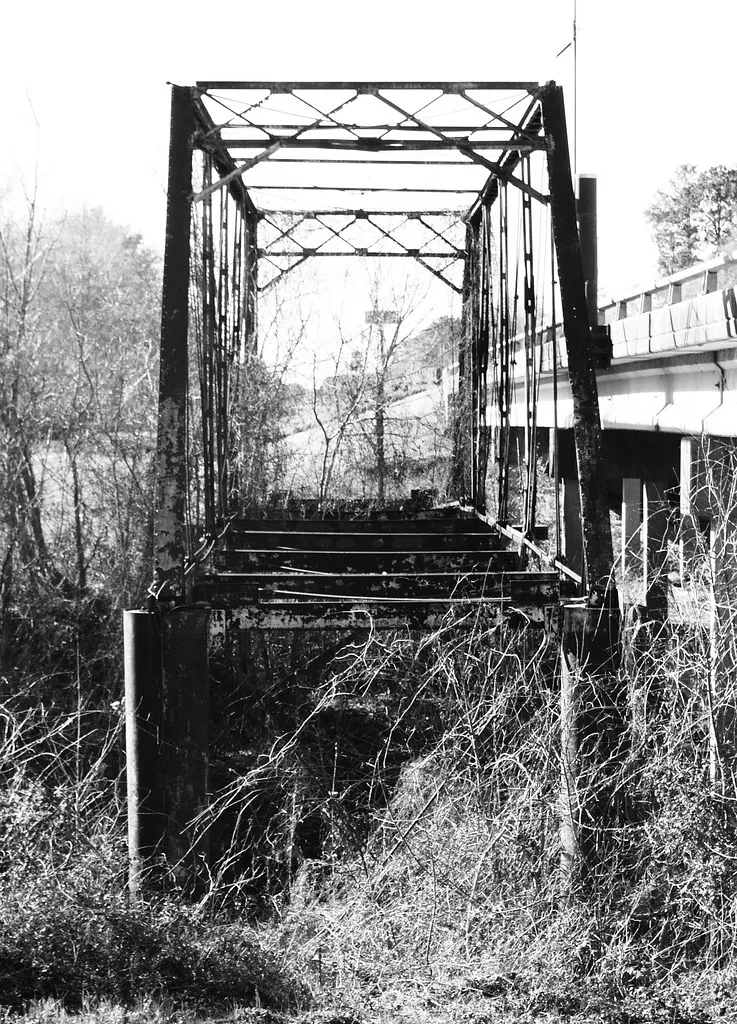Ossature métallique d’un pont abandonné sans tablier au milieu des broussailles.