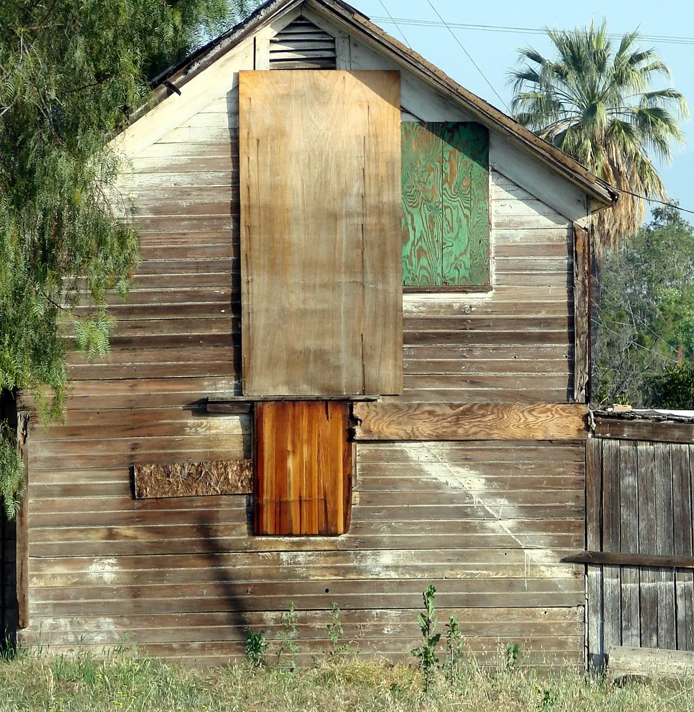 Façade d’une ancienne grange de bois aux ouvertures bouchées par des panneaux.