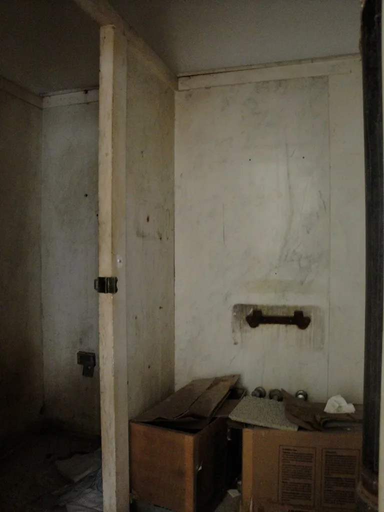 Ancienne salle d’eau vide avec cloisons défraîchies et cartons.