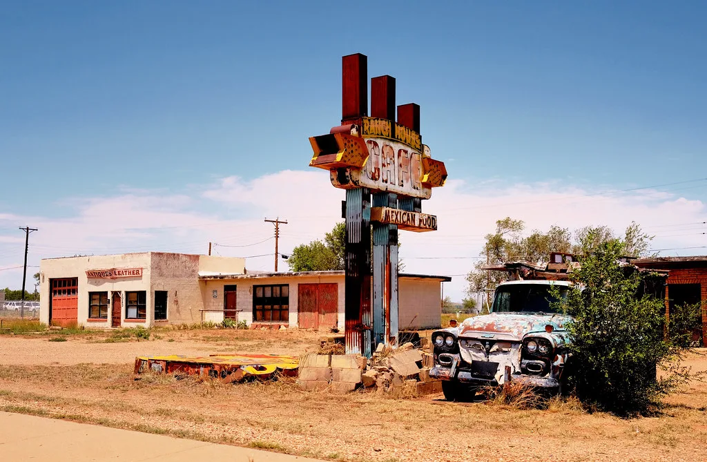Former roadside cafe with sealed openings, a rusty sign and an overgrown truck.