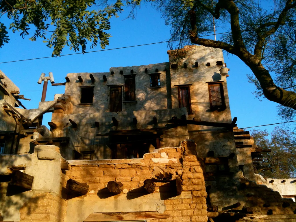 Ruins of a multilevel earthen building with collapsed walls and projecting wooden beams.