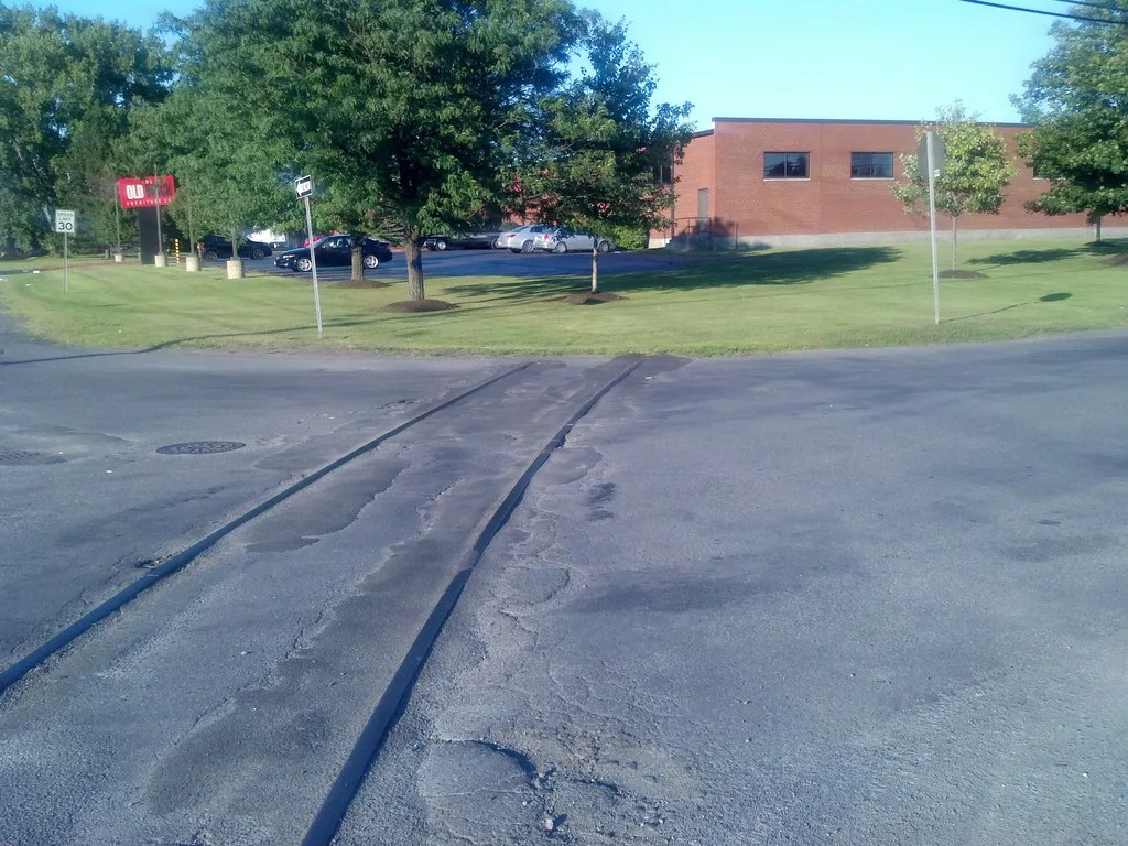 Vestiges de rails dans une chaussée devant une pelouse.