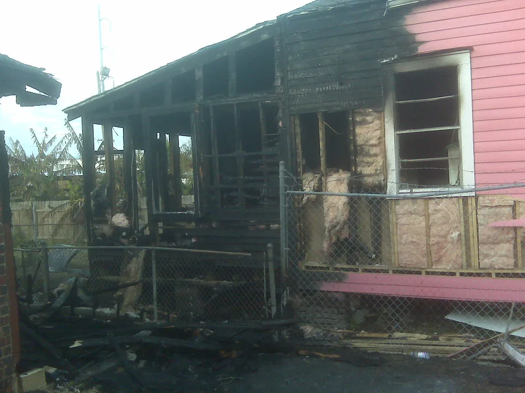 Burned and gutted wooden house behind a wire fence.