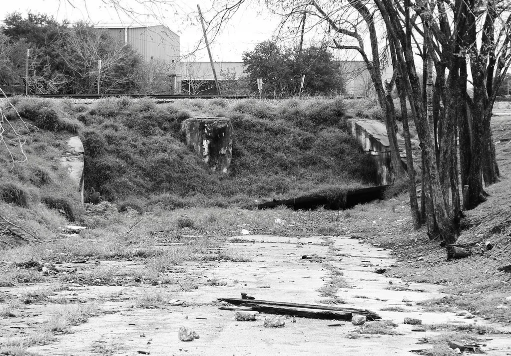 Concrete remains on a cracked weed-covered slab at the foot of a railway embankment.