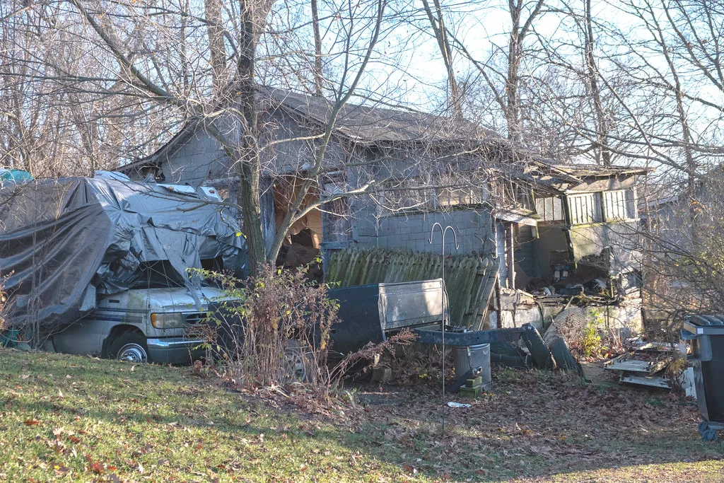 Maison délabrée partiellement effondrée derrière des arbres et des débris.
