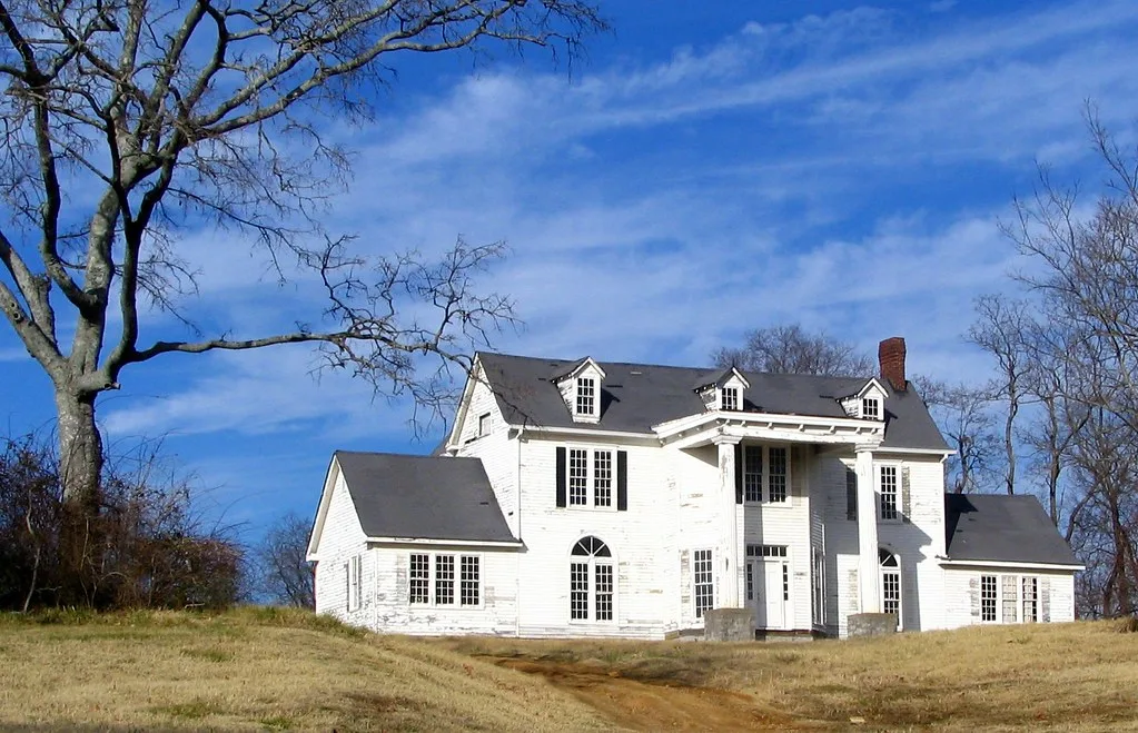 Large white house with columns on grassy ground.
