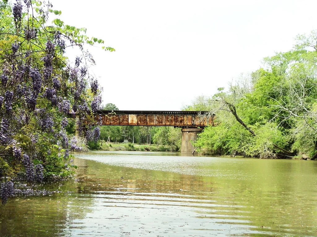 Ancien pont métallique rouillé au-dessus d’une rivière bordée d’arbres.