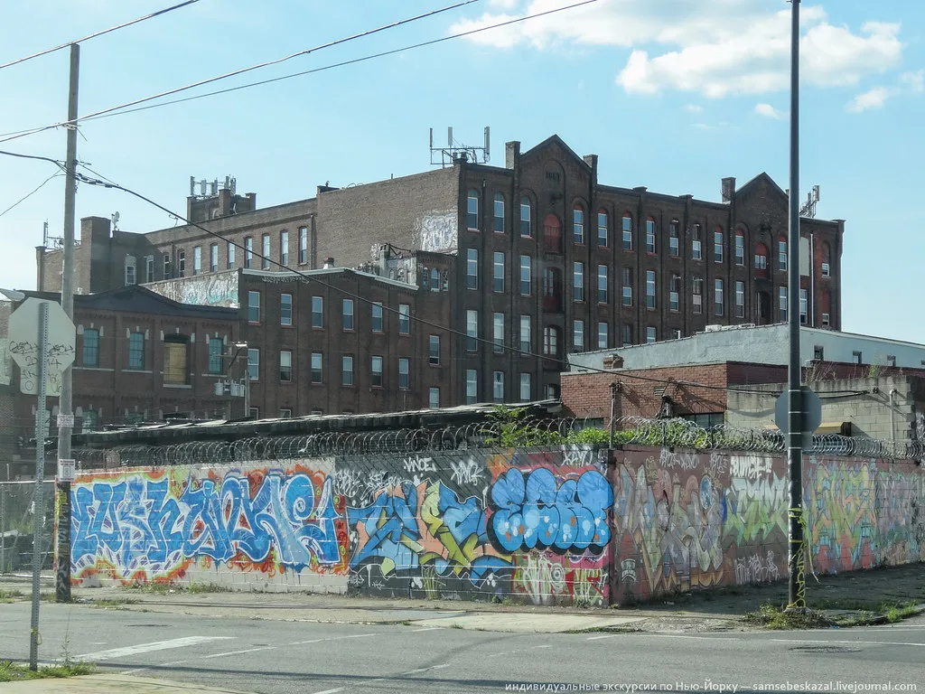 Low industrial ruins behind a graffiti-covered wall in front of large brick buildings.