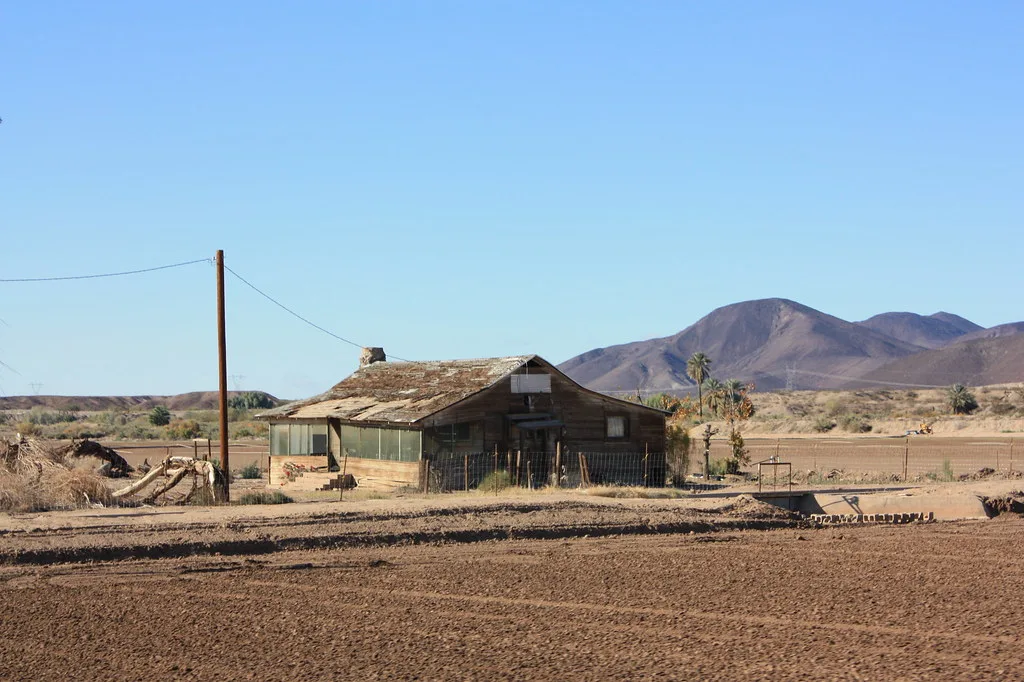 Ancienne maison de bois au toit abîmé dans un paysage désertique.
