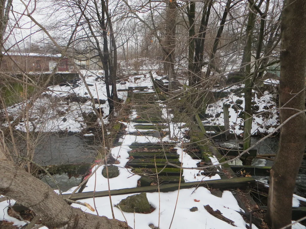 Snow-covered remains of a decaying wooden footbridge among trees.
