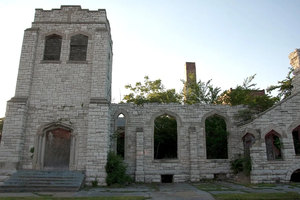 Église en ruine avec tour carrée et ouvertures envahies de végétation.