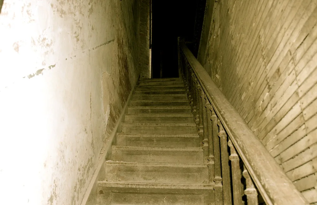 Old staircase between deteriorated walls with a wooden handrail.