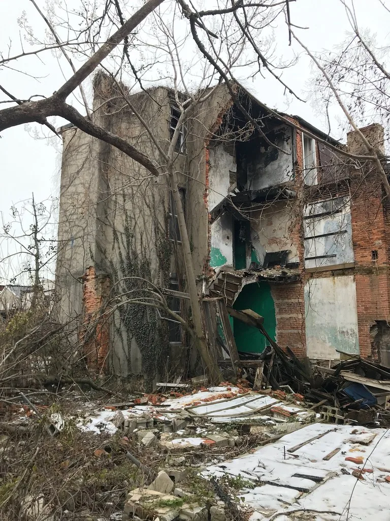 Maison de briques partiellement effondrée avec débris et neige au sol.