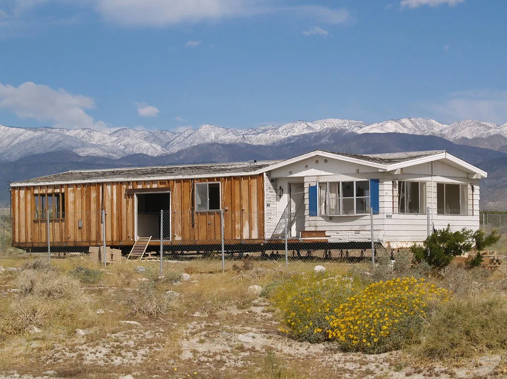 Old dwelling with torn-off cladding in front of snow-covered mountains.