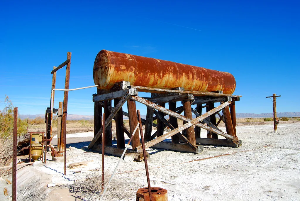 Grand réservoir cylindrique rouillé posé sur des tréteaux de bois usés dans un paysage aride.