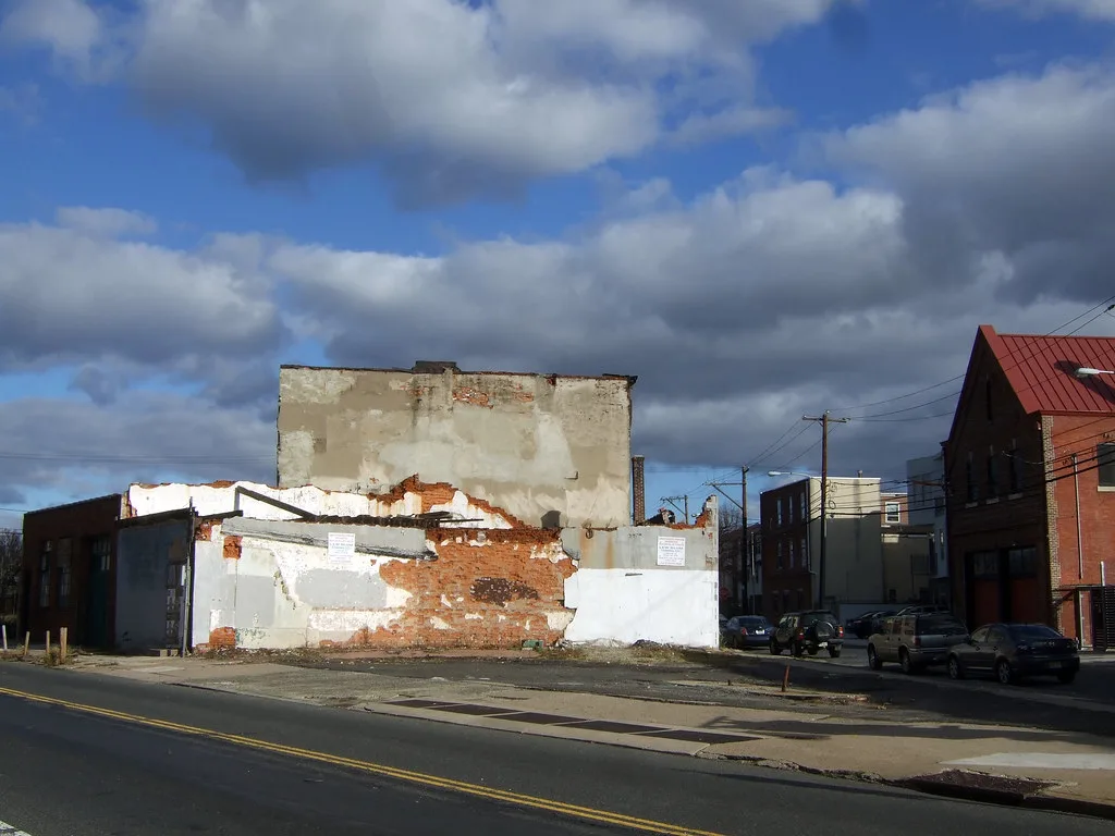Ruined brick walls with torn-off render beside a street.
