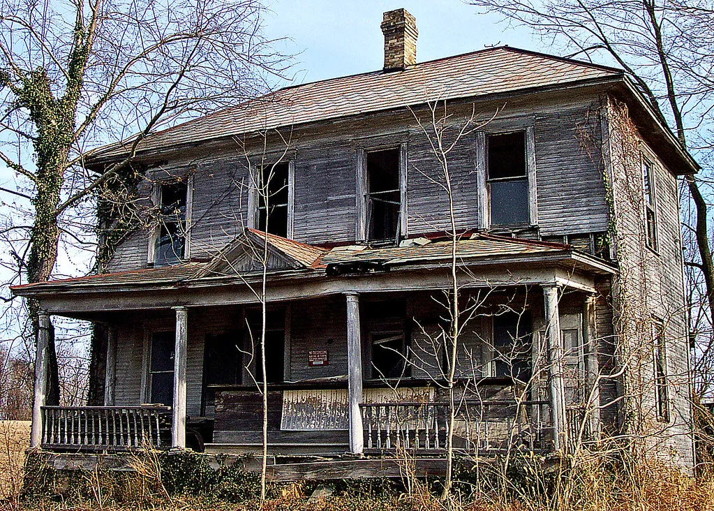 Ancienne maison de bois aux fenêtres vides et au porche dégradé.