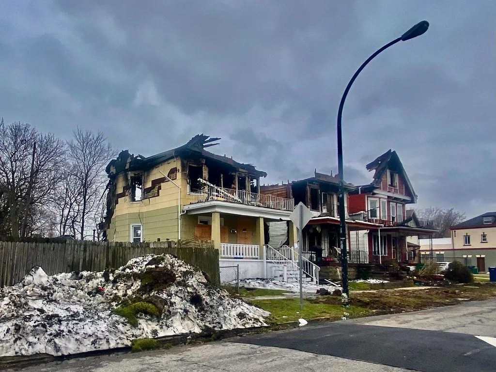 Maisons jaune et rouge brûlées aux charpentes exposées près de tas de neige.