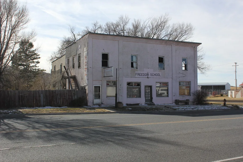 Neglected building bearing Freedom School lettering, with broken upper windows and an exterior wooden staircase.