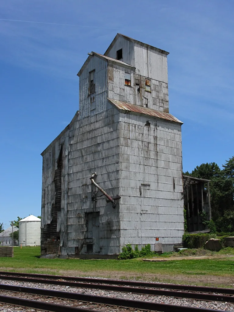 Old grain elevator with deteriorated cladding beside a railway.