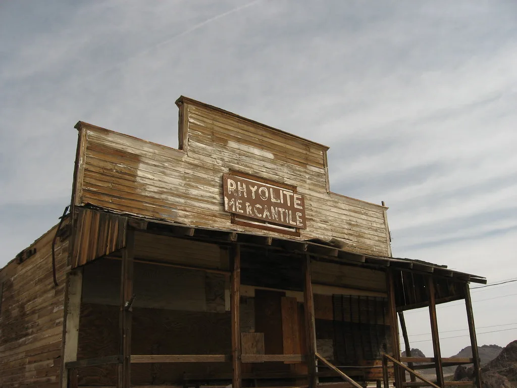Old wooden shop with barricaded openings and a weathered porch beneath a gray sky.