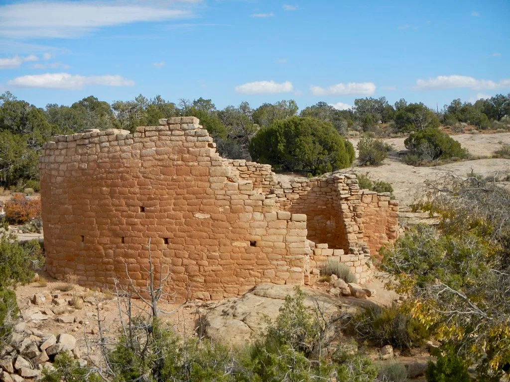 Ruined pale stone walls among shrubs in an arid landscape.