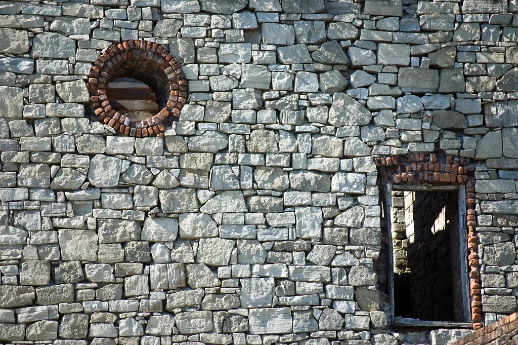 Stone wall with round and rectangular openings edged in brick.