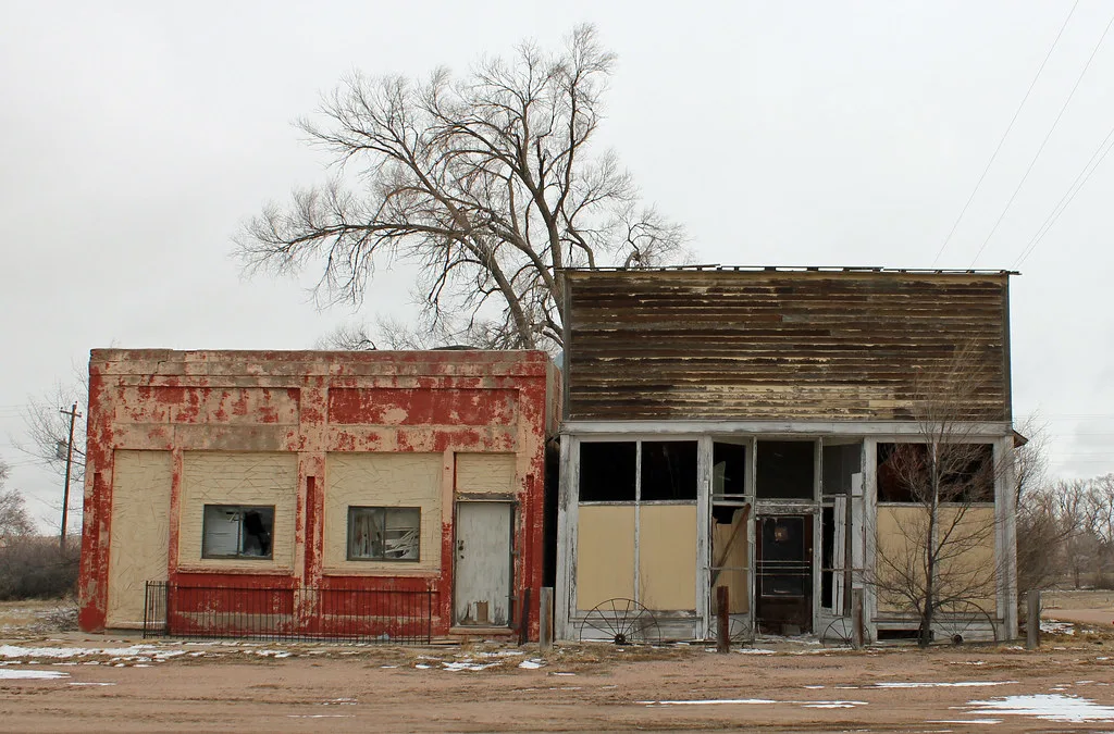 Two abandoned shops with shattered windows and red and brown facades.