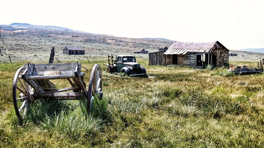 Anciennes cabanes de bois, charrette et camion dans une prairie.