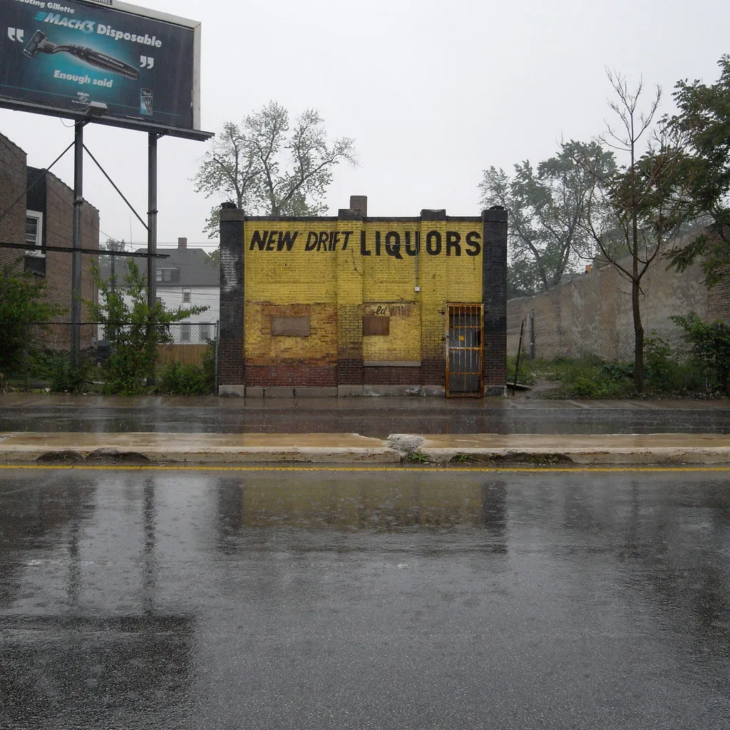 Small yellow New Drift Liquors shop with bricked-up storefront windows and a barred door.