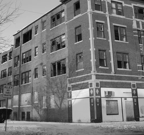 Abandoned four-story brick building with broken windows and boarded ground-floor openings.