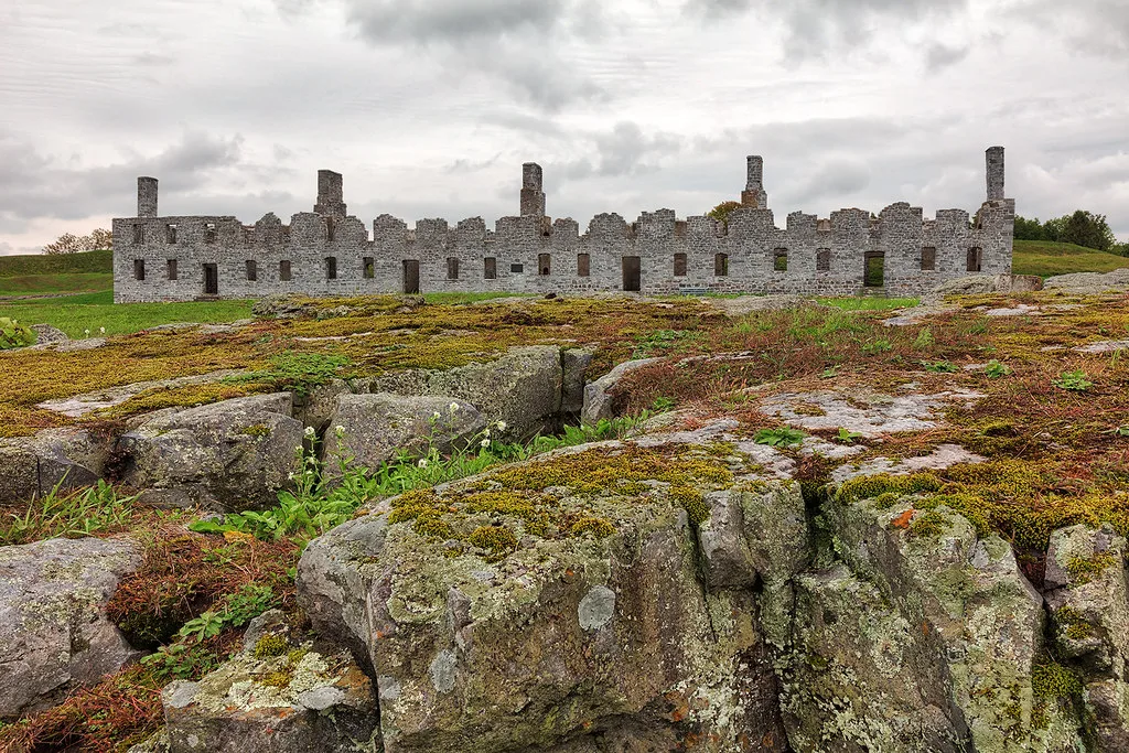 Long ruined stone walls and chimneys beyond rocky ground.