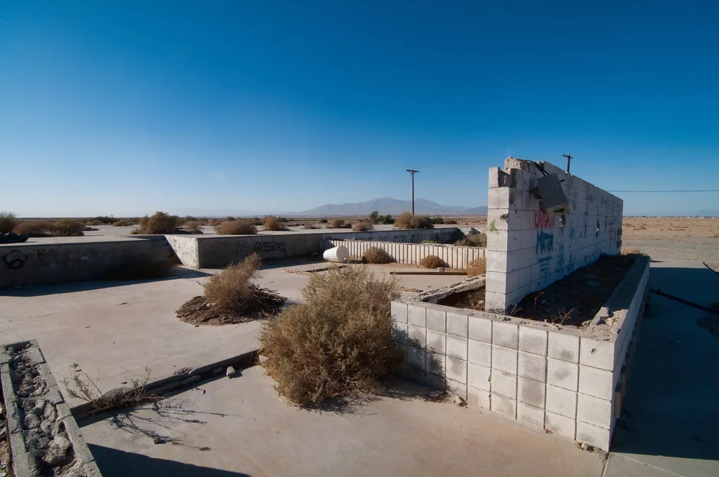 Vestiges de murs et dalles de béton sur un terrain désertique.